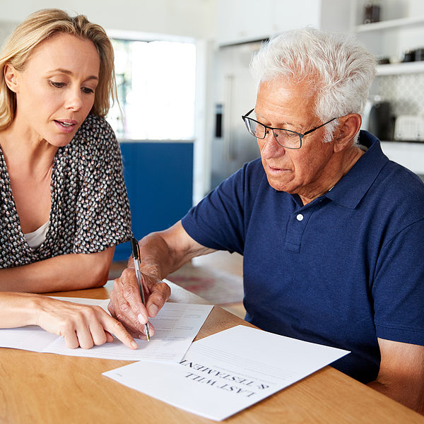 Woman Helping Senior Man To Complete Last Will And Testament At Home