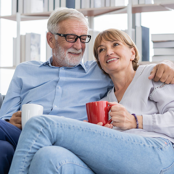 Happy morning, caucasians senior lover couple family. Mature, adult retired man, woman drinking coffee, tea together, embracing, hugging on sofa, couch at home. Pleasure husband and wife lifestyle.